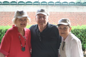 Three elderly people smiling outdoors, wearing hats.